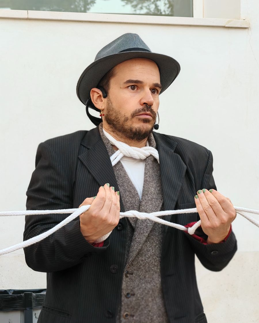 Charlie, con sombrero y chaleco, hace un juego de magia con una cuerda al cuello